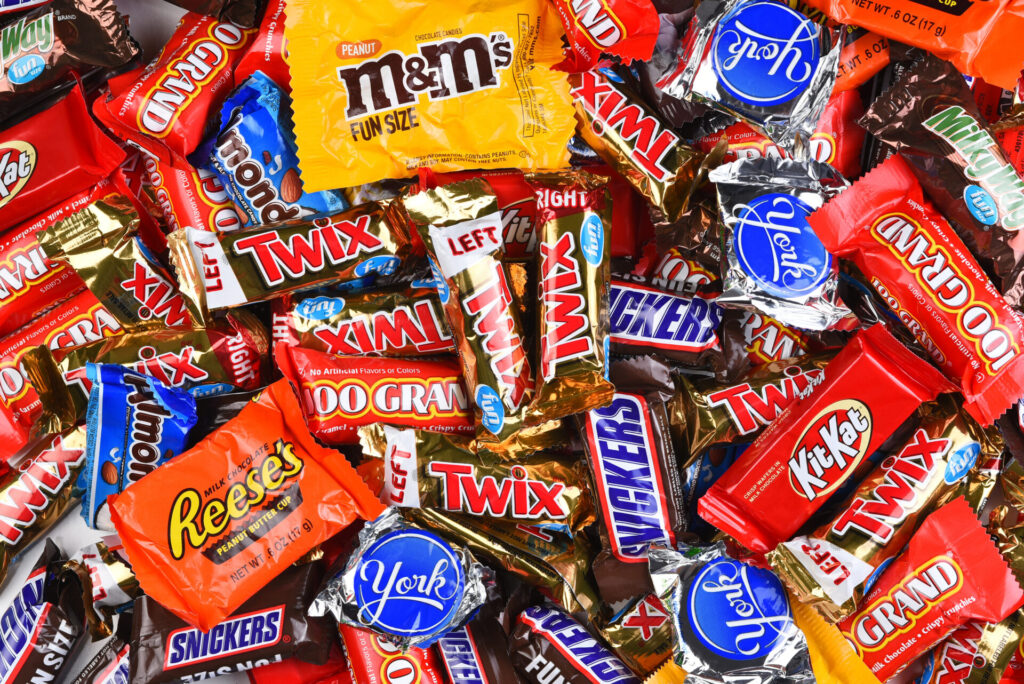 Assorted Halloween candy wrappers including M&Ms, Twix, Snickers, KitKat, Reese's, and other chocolate and peanut candy brands